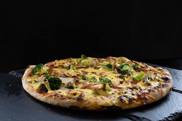 Close-up of a slice of Tandoori Chicken Pizza showing juicy chicken, melted cheese, and colorful vegetables