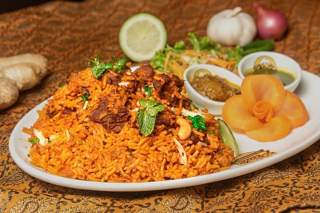 Delicious plate of biryani garnished with fried onions, mint leaves, and lemon wedges.