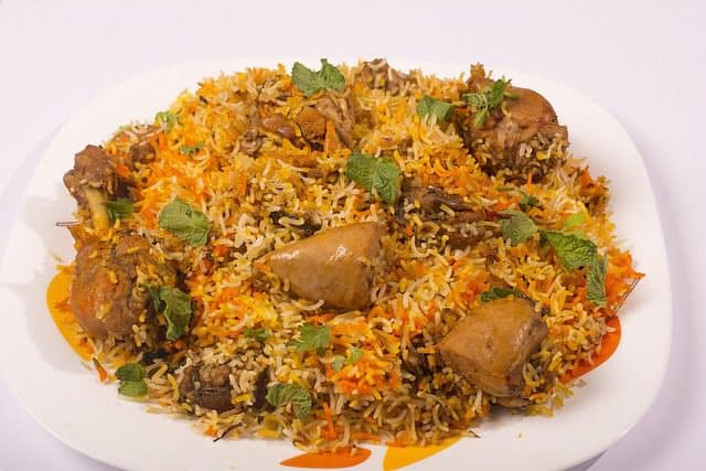 Traditional dum biryani cooking in a pot with layers of rice, chicken, and spices.